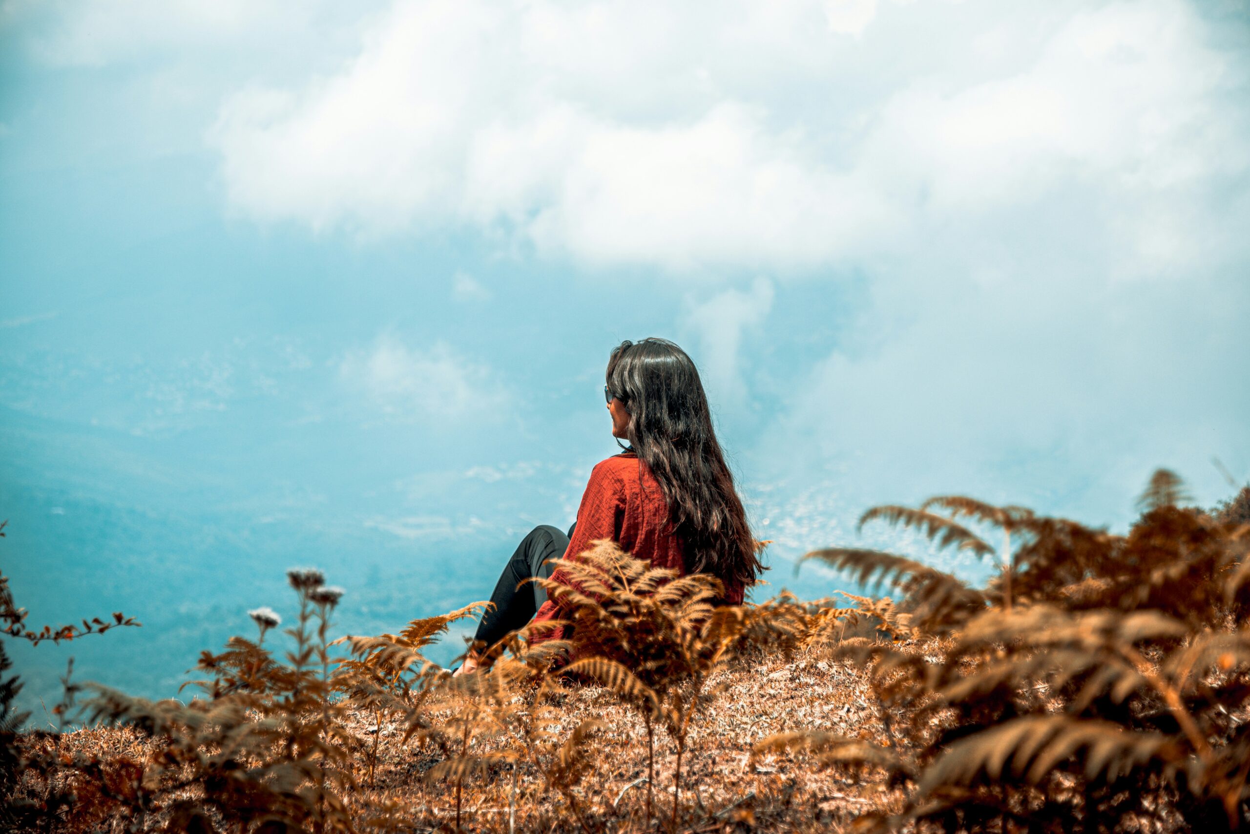 Frau sitzt ruhig in der Natur und blickt in die Ferne – ein Moment der Reflexion, in dem sie ihre Identität und Gottes Wahrheit erkennt.