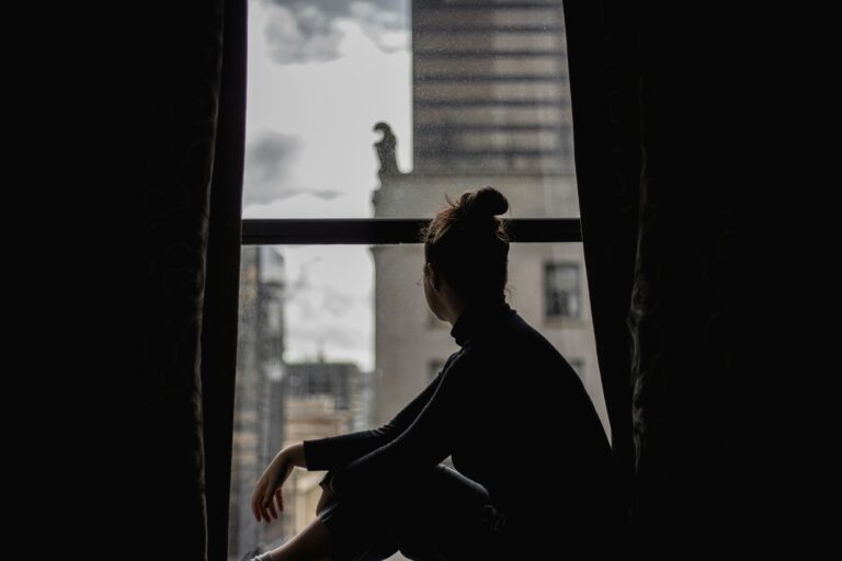 Woman sitting alone by a window looking outside — symbolizing inner pain, loss, and loneliness.