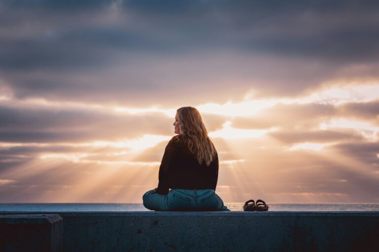 Frau sitzt vor einem leuchtenden Himmel am Meer – symbolisch für Hoffnung, Heilung und Gottes Frieden mitten im Schmerz.