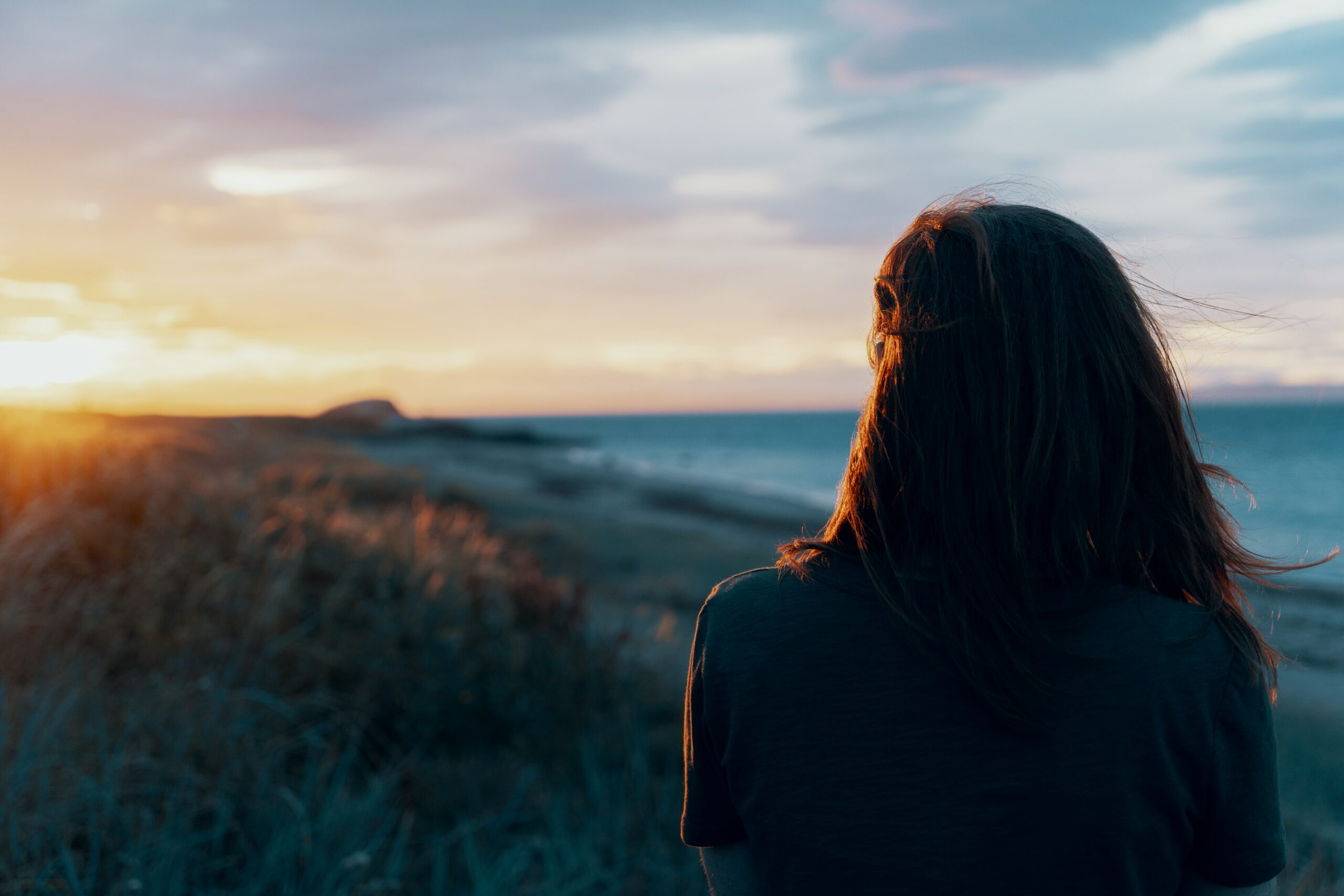 A person looks at the ocean at sunset, reflecting on their journey with God.