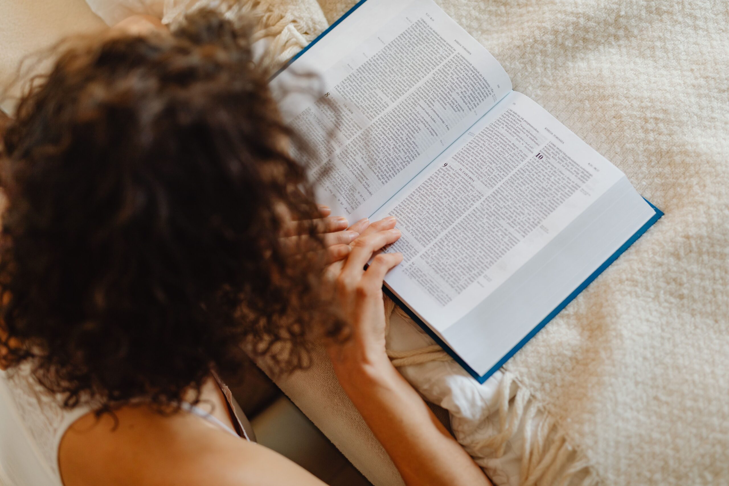 Eine Frau liest auf ihrem Bett in einer geöffneten Bibel und sucht Gottes Antwort in einer schweren Zeit.