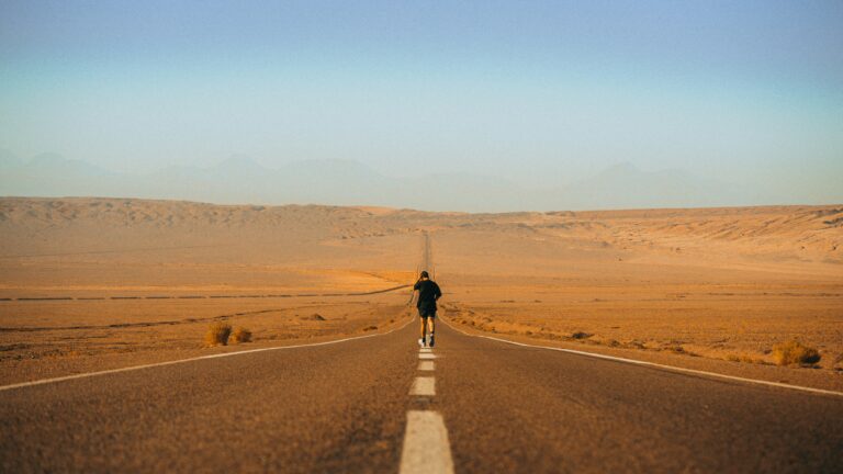 God is working in silence — Part 1 3 A man walks alone on a long road through a vast desert landscape.